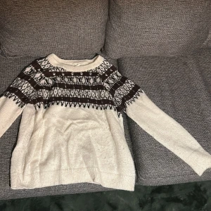 Vit stickad tröja med pärlor och mönster - Säljer en vit stickad tröja med brunt och svart mönster upptill. Tröjan har långa ärmar och är dekorerad med pärlor och små stenar för extra detalj. Perfekt för dig som vill ha något unikt och mysigt till hösten eller vintern.