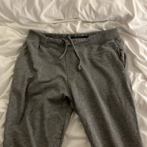 Grå mjukisbyxor Tiger of Sweden M - Grå mjukisbyxor från Tiger of Sweden i storlek M. Byxorna har snörning i midjan, sidofickor och bakfickor. Tillverkade i mjukt bomullsmaterial med normal passform, perfekt för chill dagar. Snygg och enkel design som funkar till allt. Knappen har lossnat men snörena fungerar bra!