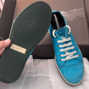 Turkosa sneakers från Lanvin - Säljer ett par snygga turkosa sneakers från Lanvin med vit sula och vita snören. Skorna är tillverkade i mjuk mocka och har en klassisk rund tå och platt sula. Perfekt för dig som gillar färg och vill sticka ut med ett exklusivt märke.