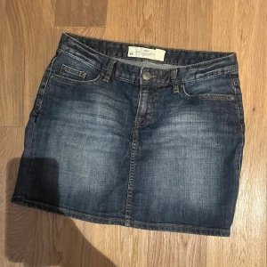 Mörkblå jeanskjol från H&M - Klassisk mörkblå jeanskjol från H&M med fem fickor och knappstängning framtill. Kjolen har en rak passform och är tillverkad i denim med snygga slitningar för en avslappnad look. Perfekt att matcha med sneakers eller boots.