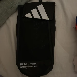 Adidas Predator målvaktshandskar junior - Säljer ett par Adidas Predator målvaktshandskar för juniorer. Handskarna har en cool kombination av blått, vitt och orange med breda kardborreband för extra stöd. Insidan är vit med URG 2.0-tryck, och utsidan har Adidas klassiska ränder. Perfekta för fotbollsmålvakter!