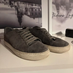 Grå mocka sneakers från Arigato - Snygga grå sneakers från Arigato i mjuk mocka med rund tå och platt vit sula. Skorna har klassisk snörning och en stilren design som passar till det mesta. Perfekta för dig som gillar minimalistisk stil och vill ha ett par schyssta sneakers. De är lite smutsiga men går lätt att ordna. Pris kan diskuteras!