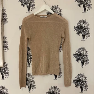 Glittrig beige tröja från NA-KD - Snygg beige långärmad tröja från NA-KD i storlek XS. Tröjan har en glittrig finish som ger den extra attityd och är figurnära med rund hals. Perfekt för dig som vill sticka ut med en stilren men ändå festlig look.