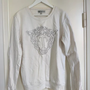 Tiger of Sweden Sweatshirt  - Vit sweatshirt från Tiger of Sweden Jeans med ett stort broderat tigerhuvud i vitt och grått på bröstet. Tröjan har rund hals, långa ärmar och ribbade muddar vid ärmslut och nederkant. Perfekt för dig som gillar stilrena detaljer och snygga loggor.Tröjan är i bra bruksskick inget som påverkar helhetsintrycket.