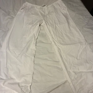 Vita linnebyxor från 157, storlek M - Vita linnebyxor från 157 med avslappnad passform och resår i midjan. Byxorna har raka ben och är tillverkade i ett lätt och luftigt linnematerial, perfekta för varma dagar. Klassisk och enkel design som är lätt att matcha. Dem är uppsydda och har ett litet hål längst ner