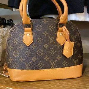 Lejla  handväska - Säljer en klassisk handväska mörkbrunt och beige. Väskan har rundad form, två handtag i ljusbrunt skinn och detaljer i guld. Perfekt storlek för det viktigaste och snygg att bära till alla outfits.