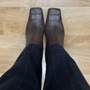 Bruna läder boots med fyrkantig tå - Snygga bruna boots i skinn med fyrkantig tå och markerad blockklack. Dragkedja på sidan för enkel påtagning och dekorativ söm längs skaftet. Köpta vintage, begränsat använda. Upplever dem som en stor/lång storlek 39, rymliga vid tårna pga fyrkantiga tån.