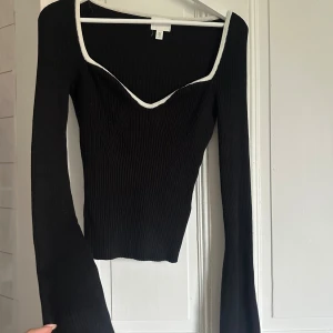 Svart ribbad långärmad topp med vit kant - Säljer en svart ribbad långärmad topp med vit kant runt den djupa v-ringningen. Säljer likadan i brun också! Storlek M