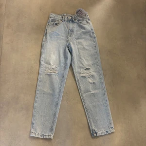 Ljusblå mom jeans från FB Sister XS - Ljusblå mom jeans från FB Sister i storlek XS. Högmidjade med raka ben och slitna detaljer på båda benen. Klassisk femficksmodell i mjuk bomullsdenim. Perfekta för en avslappnad och trendig look. Nya helt oanvända 