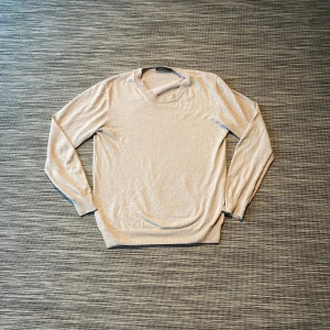 Beige stickad tröja från Oscar Jacobson - Snygg beige stickad tröja från Oscar Jacobson, tillverkad i Italien. Tröjan har rund hals, ribbade muddar och långärmad design. Perfekt för dig som gillar stilrena och klassiska plagg med mjuk känsla.