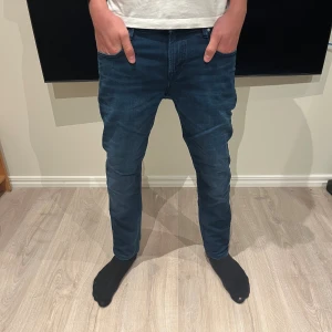 Blå jeans från Scotch & Soda - Säljer ett par snygga blå jeans från Scotch & Soda, modell Amsterdams Blauw. Jeansen har klassisk femficksdesign, slim fit och coola detaljer med färgade korsstygn på bakfickan. Perfekt passform och stilren look.