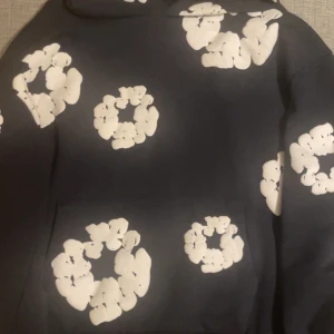 Denim Tears hoodie - Svart hoodie från Denim Tears med stora vita blommiga cirkeltryck över hela tröjan. Klassisk huva och känguruficka framtill. Perfekt statement-plagg för dig som vill sticka ut med cool design. Har använts 1-4 gånger!
