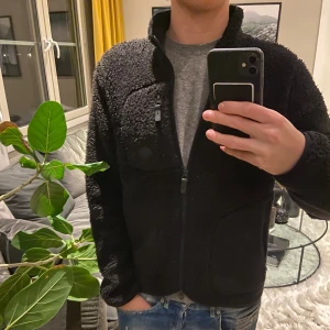 Svart teddyjacka j.lindeberg  - Tjena ! Säljer en mysig svart teddyjacka med hel dragkedja framtill och hög krage. Jackan har en fluffig yta och praktiska fickor, perfekt för att hålla värmen. Passar dig som gillar en chill och avslappnad stil. Kontakta för fler frågor 