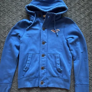 Hollister hoodie med knappar - En archived hollister hoodie med knappar. Den är i storlek M och modellen på bilden är 182 cm lång och väger 70 kg. Hoodien är nästan aldrig använd och i perfekt skick inga defekter 9,2/10✅. Hör av dig om du har några frågor