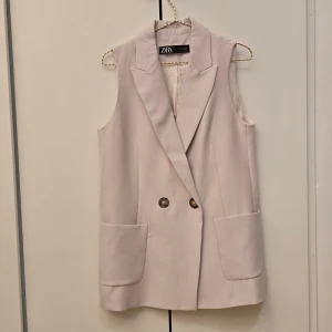 Zara beige kostymväst - 🌷FÖRST TILL KVARN!🌷En längre kostymväst från Zara i ljusbeige färg. Rak och lös men strukturerad tyg och krage. Stängs med knapp på insidan och en i utsidan, storlek M. Två fickor på vardera sida av västen. Endast använd få gånger. VILL BLI AV MED ASAP!