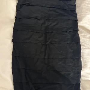 Svart bandeau-topp från Gina Tricot - Säljer en svart topp från Gina Tricot med lager-på-lager effekt. Klänningen har en enkel och stilren design som passar perfekt till många olika tillfällen. Mjuk och bekväm att bära.