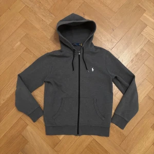 Grå Ralph Lauren Zip Hoodie - Säljer min Ralph lauren hoodie pga för liten storlek, har inte heller använts mycket. Färgen är mörkgrå och den är i storlek S. Den har inga defekter, bara att komma med prisförslag!