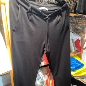 Svarta mjukisbyxor med snörning - Svarta mjukisbyxor med elastisk midja och snörning framtill. Byxorna har en avslappnad passform och sidofickor, perfekta för chill dagar eller när du vill vara bekväm. Tillverkade i mjukt material som känns skönt mot huden.