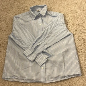 Blåvit randig skjorta från Kappahl - Snygg blå skjorta med vita ränder från Kappahl. Klassisk krage, långa ärmar och knappar fram.Skjortan är i mjuk bomull och passar till många olika outfits.