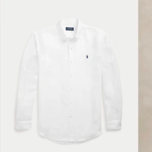 Vit linneskjorta Polo Ralph Lauren M - Vit skjorta från Polo Ralph Lauren i slim fit med klassisk krage och knappar framtill. Tillverkad i 100% linne, har lång ärm och den ikoniska blå broderade loggan på bröstet. Perfekt för dig som gillar stilren och fräsch look. Nypris 2 tusen.