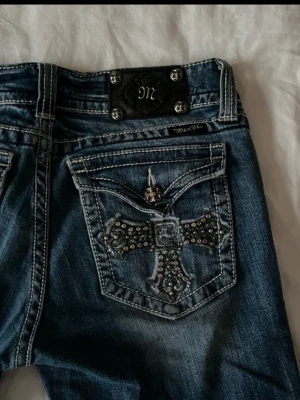 Miss Me blå jeans med gems - Säljer ett par blå bootcut Miss Me jeans med snygga detaljer och gems på bakfickan. Super snygga och I toppen skick. Jag är 168cm lång. Midjemått:42cm innerbenslängd: 85cm