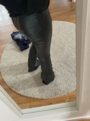 Svarta byxor i skinnimitation - Säljer ett par svarta skinnbyxor med utsvängda ben. Byxorna har fickor bak och sitter tight över höfterna. Perfekta för dig som vill ha en edgy och trendig look.
