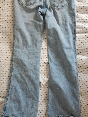 Ljusblå bootcut jeans - Säljer ett par ljusblå jeans med bootcut passform och broderade detaljer på bakfickorna. Jeansen har klassisk femficksdesign och är gjorda i denim. Perfekta för dig som gillar en avslappnad och trendig stil.