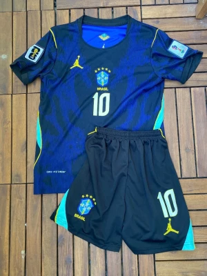 Brasilien Neymar Jr matchställ blå/gul - Snyggt matchställ för Brasilien med Neymar Jr och nummer 10. Tröjan är blå med gula detaljer, klubbmärke och tryck, och har korta ärmar. Shortsen är svarta med gula och blå detaljer samt nummer 10. Perfekt för fotbollsträning eller match. Size S