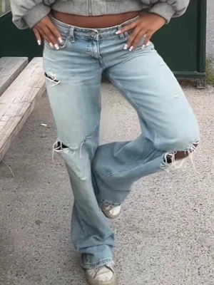 Ljusblå raka jeans - Säljer ett par ljusblå jeans med raka ben och hål på knä och lår. Jeansen har låg/medel midja och klassisk femficksmodell. Perfekta för en avslappnad och trendig look. Materialet är denim i bomull.