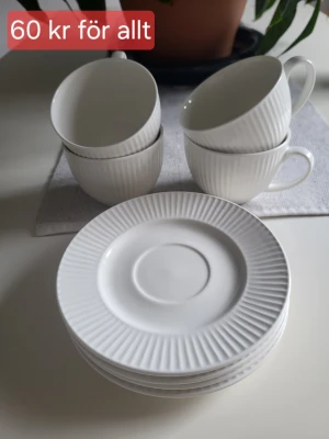 Vita koppar och fat från Kotikulta - Säljer ett set med fyra vita koppar och fyra matchande fat från Kotikulta. Allt har ett stilrent räfflat mönster och är tillverkat i porslin. Kopparna och faten är både mikrovågs- och diskmaskinssäkra. Perfekt för fika eller te.
