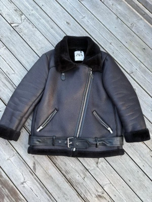 ZARA  Jacket - This is a ZARA faux shearling aviator jacket in size Medium. It features a black faux shearling lining, an asymmetrical front zipper, two zippered side pockets, a belted waist, and a wide collar. The jacket is designed for warmth and style, perfect for colder weather.
