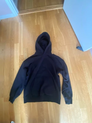 Svart hoodie från Cubus - En enkel svart hoodie med huva och stor magficka framtill. Hoodien har ribbade muddar vid ärmslut och nederkant. Perfekt för en avslappnad och chill stil. Materialet ser ut att vara mjukt och bekvämt, troligen bomullsblandning.