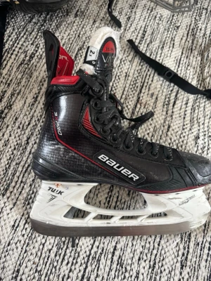 Bauer Vapor X hockeyskridskor - Säljer ett par Bauer Vapor X hockeyskridskor i svart med röda och vita detaljer. Skridskorna har robust snörning, tålig plastkappa och vita TUUK-stålblad. Perfekta för dig som vill ha grym kontroll och fart på isen. Jätte bra