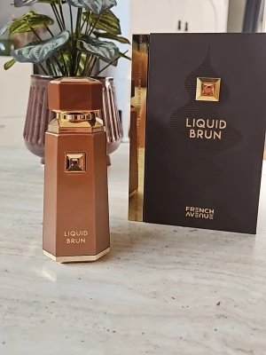 Liquid Brun parfym från French Avenue - Liquid Brun parfym från French Avenue i en elegant brun och guldfärgad flaska med geometrisk form och exklusiva gulddetaljer. Flaskan har en dekorativ fyrkantig sten på framsidan och matchande förpackning. Minst 95ml kvar.