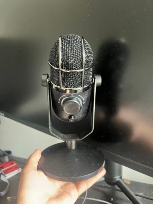 Svart USB-mikrofon med stativ - Säljer en svart mikrofon med robust metallstativ och rattar för justering. Mikrofonen har en klassisk rund form och medföljer en lång USB-kabel. Perfekt för streaming, gaming eller podd. Snygg design med metallgaller och mattsvart finish. Är i bra skick har inga problem med den alls👌