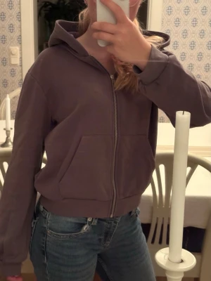 Grå zip hoodie med huva - En enkel och snygg lila hoodie med dragkedja framtill och stor ficka på magen. Hoodien har huva och ribbade muddar vid ärmslut och nederkant. Perfekt till jeans eller mjukisbyxor. Materialet känns mjukt och bekvämt.