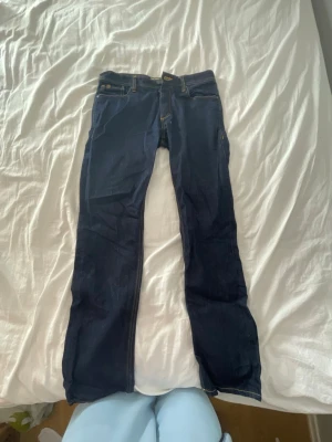 Mörkblå jack&jones jeans  - Säljer ett par mörkblå skinny jeans med klassiska fem fickor och snygga kontrastsömmar i gult. Jeansen har normal midja och dragkedja med knapp framtill. Perfekta för dig som gillar en enkel men stilren look. Storlek: 33/32