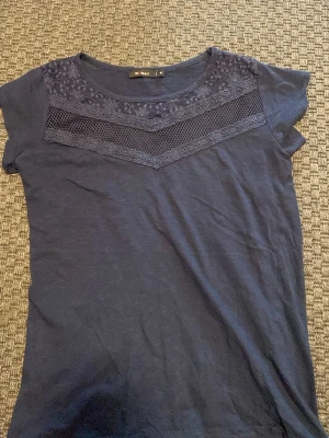 Mörkblå t-shirt med spetsdetaljer - Mörkblå t-shirt med korta ärmar och spetsdetaljer över bröstet. Står storlek M men skulle säga att det är en XS