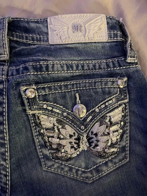 Miss Me jeans med paljettvingar - Säljer ett par blå bootcut/flare Miss Me jeans med snygga detaljer. Köpta för ca 2000. Bakfickan har broderade vingar med silverpaljetter och nitar. Jeansen har kontrastsömmar, låg midja och klassisk femficksmodell. Perfekta för dig som gillar statement-plagg!