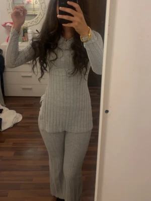 Grått ribbat två delat-set - Mysigt loungewear-set i ljusgrått med ribbad struktur. Setet består av en långärmad topp med rund hals och långa byxor med lätt utsvängda ben. Perfekt för chill dagar hemma eller när du vill vara bekväm men ändå snygg. Tröjan är storlek xs och byxorna i petite xs