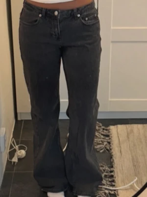 Mörkgrå bootcut jeans med fickor - Säljer ett par mörkgrå bootcut jeans med klassisk femficksdesign och extra fickor med lock bak. Jeansen har hög midja och vida ben, vilket ger en snygg siluett. Tillverkade i denim med en lätt tvättad look. Perfekta för dig som gillar trendiga och bekväma jeans.