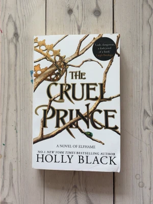 The Cruel Prince av Holly Black - En fantasyroman på engelska med vit framsida, guldfärgade grenar och en krona som dekoration. Boken är första delen i serien The Folk of the Air och handlar om maktspel, svek och magi i en farlig älvvärld. Perfekt för dig som gillar spänning och mörka sagor. Säljer för att göra plats för fler böcker. Rekommenderar denna starkt!