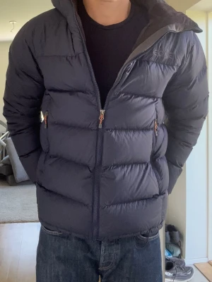  EQPE jacka - Säljer en mörkblå pufferjacka från EQPE med huva och dragkedja framtill. Jackan har två sidofickor med dragkedja och en hög krage för extra värme. Perfekt för kalla vinterdagar eller i skidbacken❄️. Klassisk quiltad design och justerbar nederkant. Pris är ej hugget i sten så tveka inte på frågor😁
