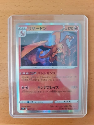 Charizard Pokémonkort japanskt - Japanskt Charizard Pokémonkort i röd och orange design med holografiska detaljer. Kortet ligger i ett genomskinligt plastfodral och har text på japanska. Perfekt för samlare eller Pokémonfans.