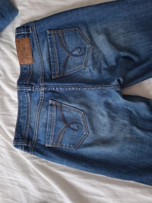 Blå vintage capris jeans från Esprit med broderi - Säljer ett par blå jeans från Esprit med snygga broderade detaljer på bakfickorna och klassisk femficksmodell. Jeansen har en mellanblå tvätt med slitningar och kontrastsömmar. Perfekta för en avslappnad och trendig look.