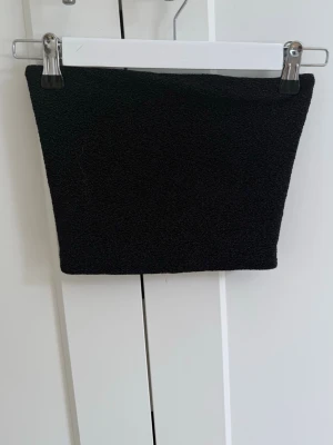 Svart tubtopp i stretchigt tyg - Säljer en enkel och stilren svart tubtopp i stretchigt, ribbat material. Toppen är axelbandslös och har en kroppsnära passform som passar perfekt till många olika outfits. Perfekt basplagg💗