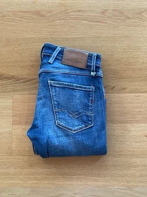 Replay Anbass - Snygga blå slim fit jeans från Replay med klassisk femficksdesign och slitna detaljer. Jeansen har en skön passform och cool tvätt med ljusare partier framtill. Perfekta för dig som gillar en modern och avslappnad stil.