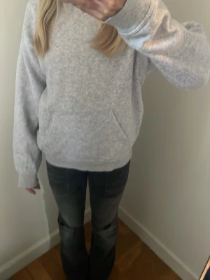 Grå basic hoodie med ficka - En enkel och stilren grå hoodie med huva och stor magficka. Tillverkad i mjukt sweatshirtmaterial som är perfekt för chill dagar. Ribbade muddar vid ärmslut och nederkant ger en skön passform. Passar till allt och är ett måste i garderoben.