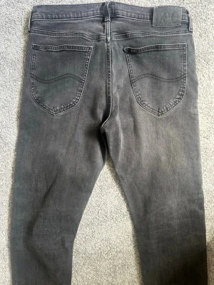 Mörkgrå jeans från Lee med raka ben - Säljer ett par mörkgrå jeans från Lee med klassisk femficksmodell och raka ben. Jeansen har en diskret tvättad look och Lee-logga på bakfickan. Perfekta till vardags för en avslappnad stil. De är i väldigt bra skick, säljer pga för små.