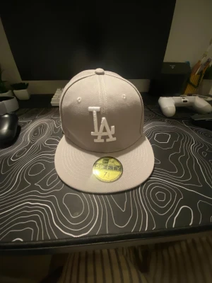 Grå LA 59FIFTY keps från New Era - Snygg grå 59FIFTY keps från New Era med LA-logga broderad framtill i vitt. Klassisk flat brim och strukturerad passform. Kepsen har officiella stickers kvar på skärmen och är tillverkad i ett slitstarkt material.